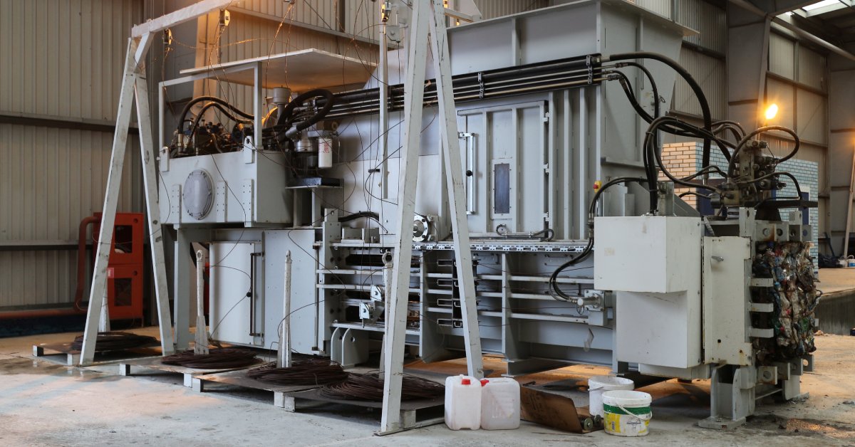 A very large hydraulic press is in the middle of a concrete floor. A few buckets are off to the side next to the equipment.