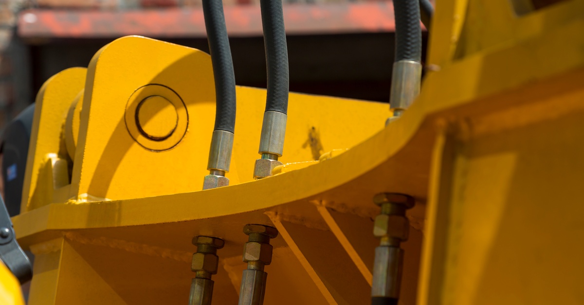 A close-up of newer hydraulic hoses and other mechanisms of yellow road machinery in an industrial setting.