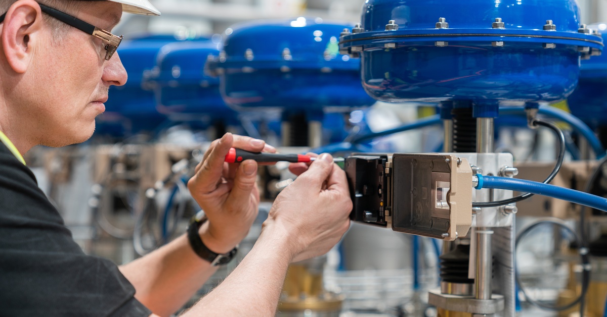 A close-up of a service engineer checking an pneumatic valve with a screwdriver in a manufacturing plant.