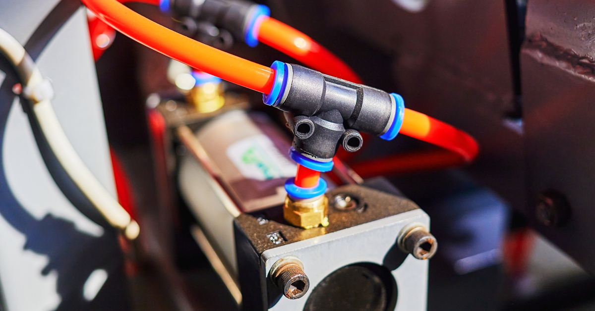 Orange duct tubing of a pneumatic system connected to the pneumatic cylinder of industrial equipment.