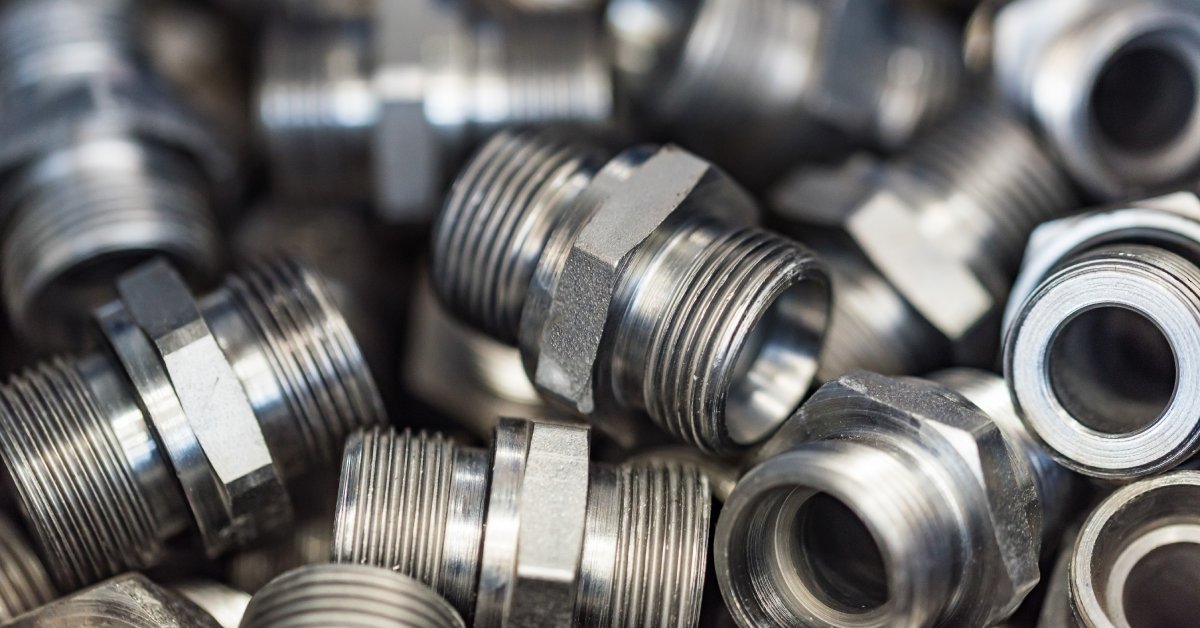 A close-up of dozens of identical silver hydraulic pipe adapters bunched up together in a large pile.