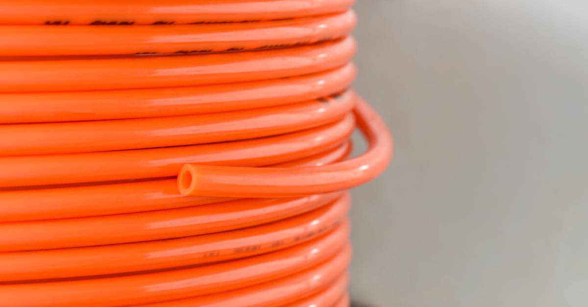 A close-up of a large coil of bright orange tubing for pneumatic system applications. A cut end hangs down the coil.