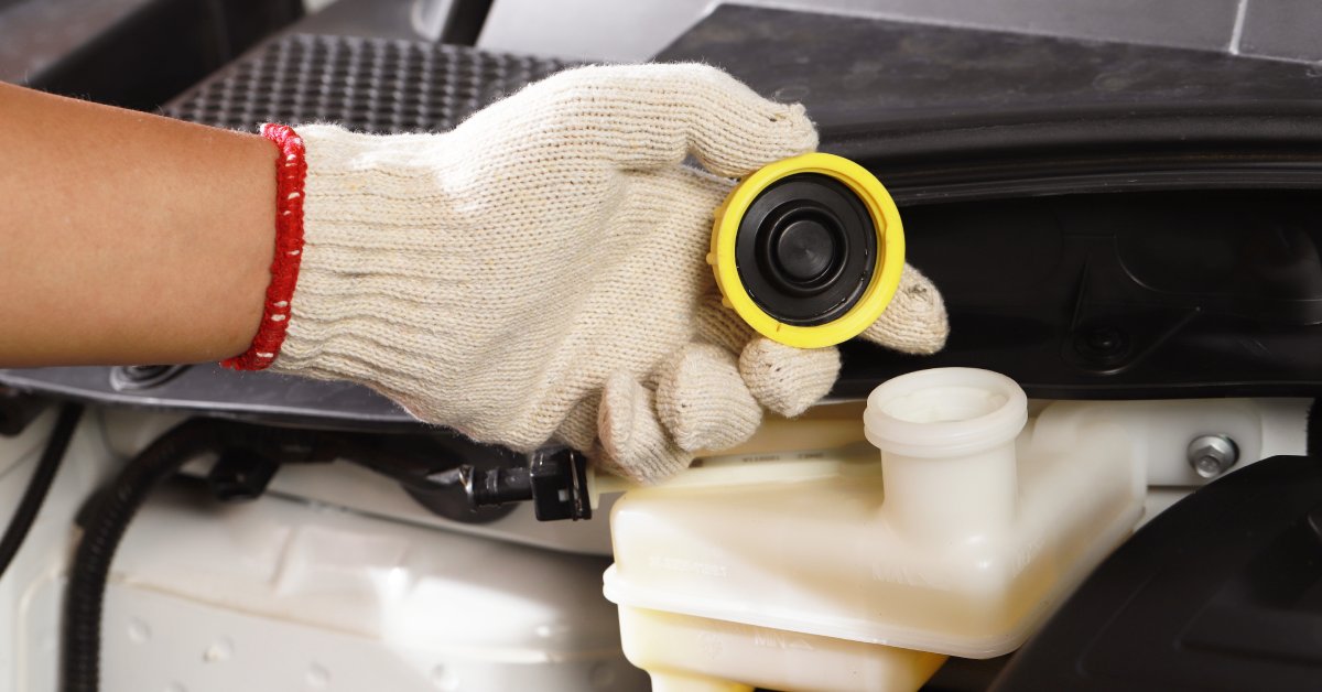 A close-up of someone's hand wearing a glove. They are holding the cap to a fluid reservoir inside a mechanical system.