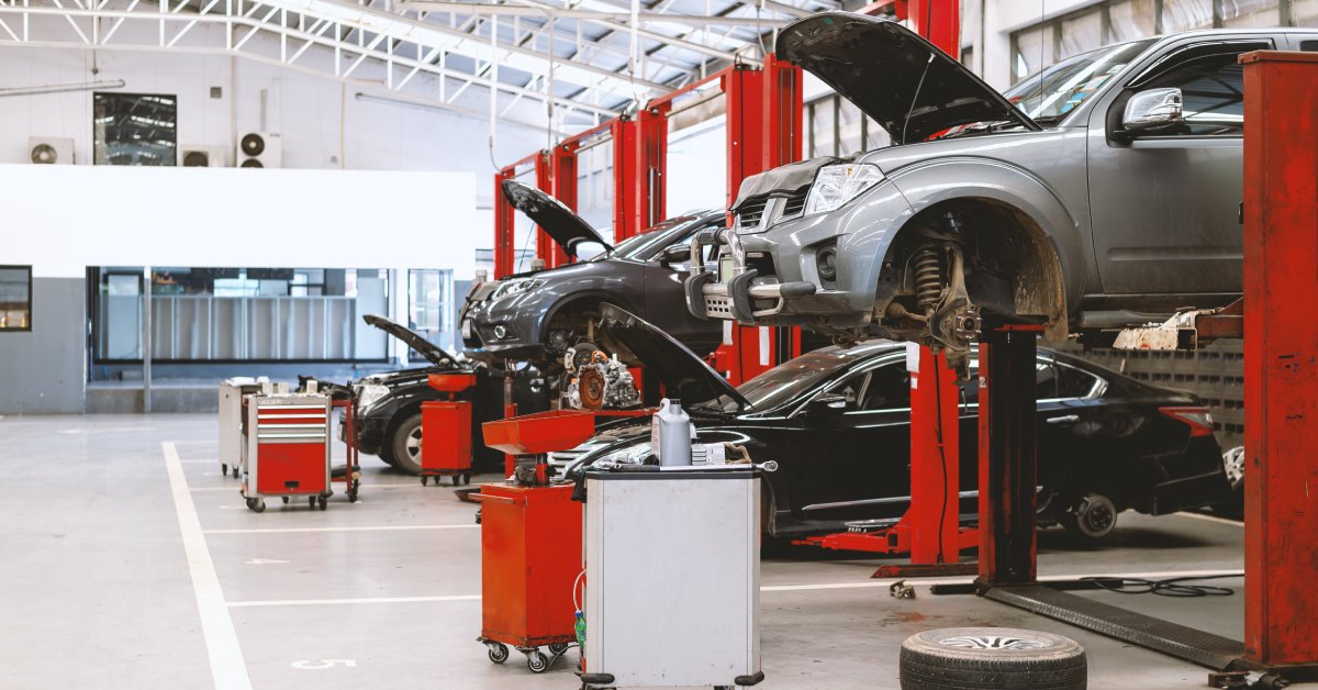The inside of an automotive garage. Two cars are on the ground while two other cars are lifted in the air by hydraulics.