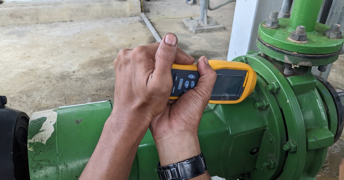Someone holds a vibration monitor against a system that is painted green and measures for noise and vibration.