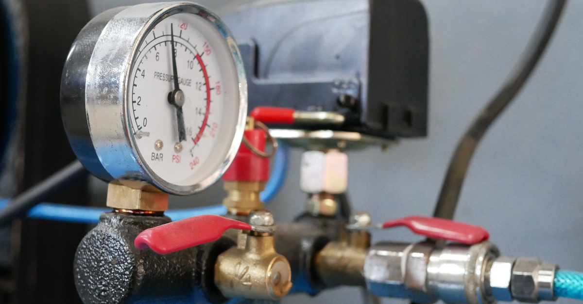 A close-up of an air compressor gauge and other components of a compressor system. The needle is in the black.