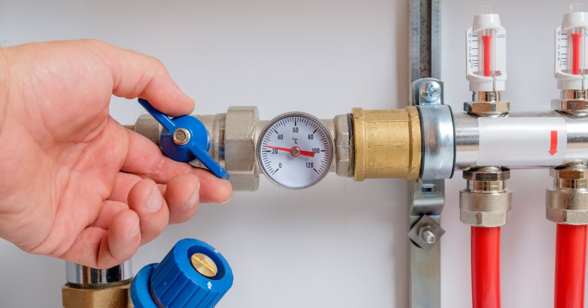 A person's left hand touches a ball valve fitted onto a supply pipeline implemented in an industrial equipment system.
