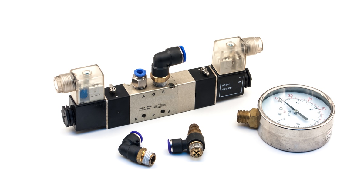 A pneumatic valve is sitting on a plain white surface. A pneumatic gauge is near it, and the needle points to zero.