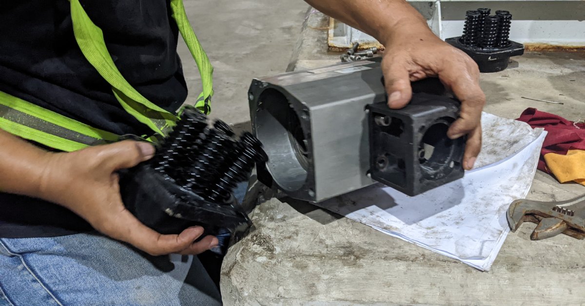A person wearing a safety belt and work clothes holds and adjusts parts of an industrial pneumatic valve.