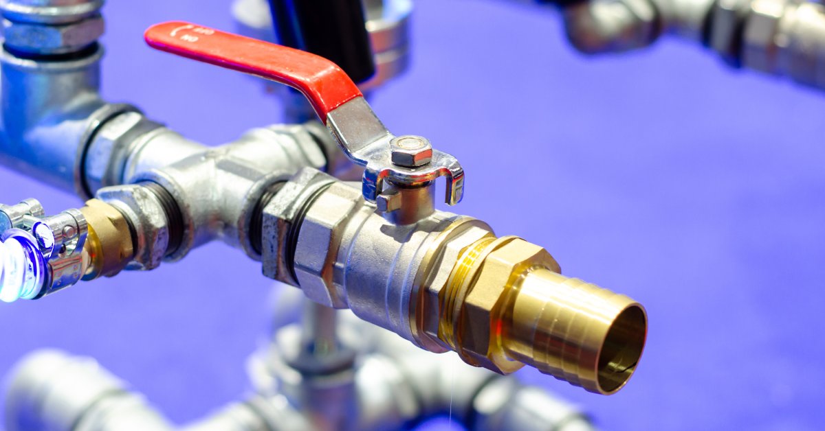 A close-up of metal piping with a ball valve on the end. There is also a red on-and-off switch with the valve.